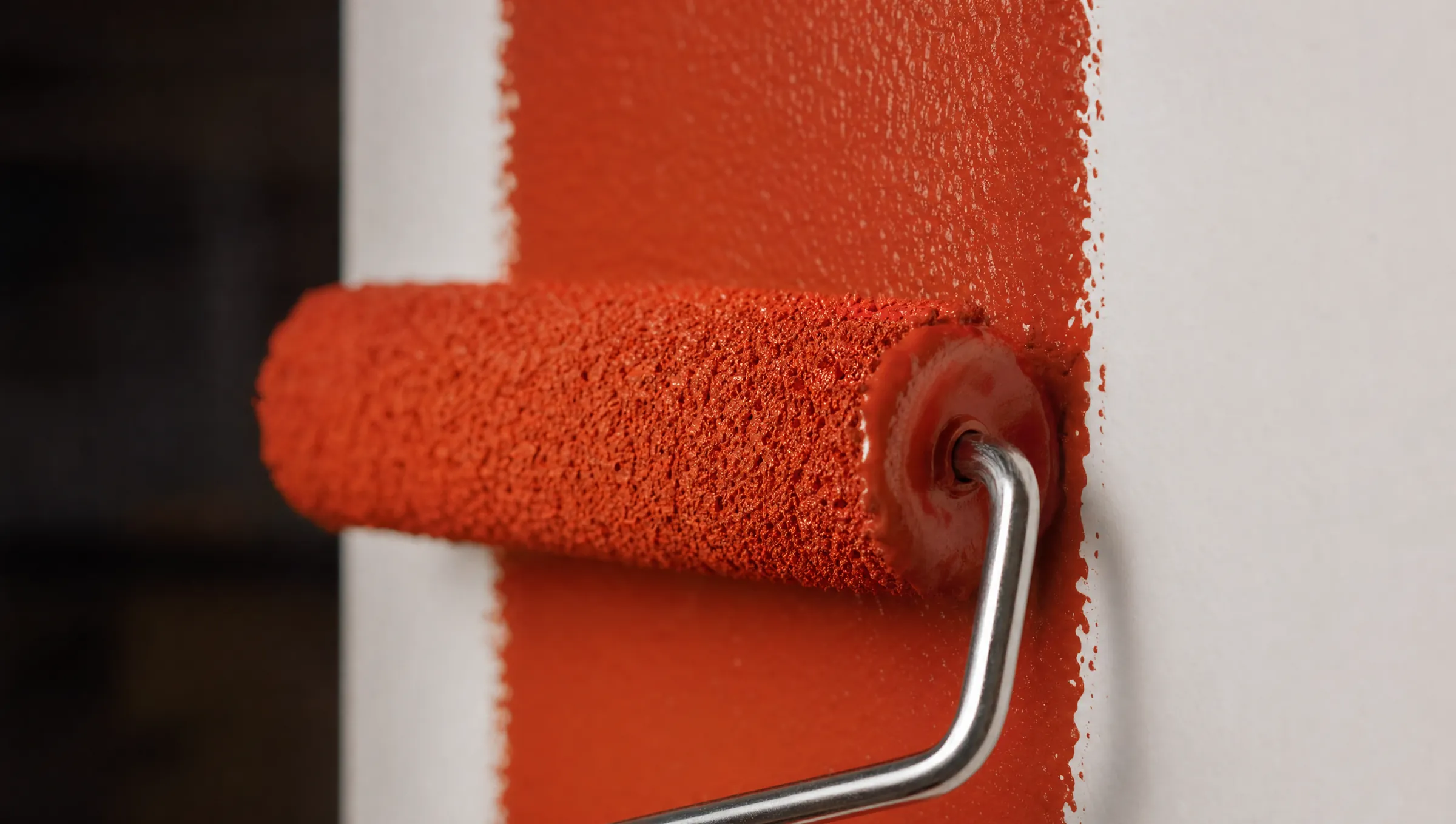 Macro photograph of a paint roller laying down a fresh stripe of brick-red paint